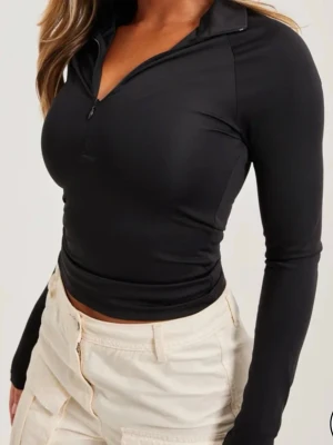 Half zip top - Svart långärmad polotopp med half zip framtill. Toppen har en tight passform och är tillverkad i ett stretchigt och glansigt material. Den är liten i storleken. Använder vanligtvis M - men denna är för kort för mig.