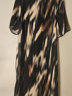 Mönstrad kortklänning i svart och beige - Cool kortklänning med abstrakt mönster i svart, beige och bruna toner. Klänningen har korta ärmar och rak passform, perfekt för dig som gillar en avslappnad men ändå trendig stil. Materialet känns lätt och smidigt mot huden.