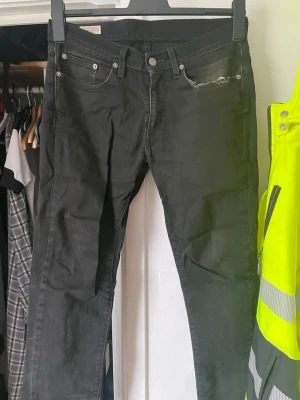 Svarta skinny jeans från Levi's - Säljer ett par svarta skinny jeans från Levi's med klassisk femficksdesign och slitning vid ena fickan. Jeansen har knappgylf och är tillverkade i stretchigt denim för en bekväm passform. Perfekta för en avslappnad och cool stil.