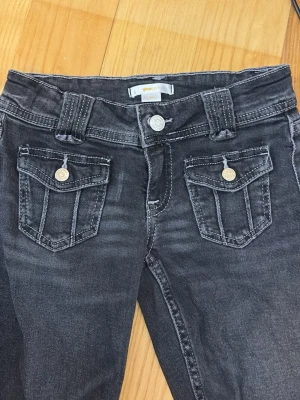 Svarta jeans med fickdetaljer - Snygga svarta jeans från Gina Tricot med raka ben och coola fickor framtill med lock och knapp. Jeansen har breda hällor och klassisk femficksdesign. Perfekta för en trendig och avslappnad look. Har INGA fläckar eller hål 