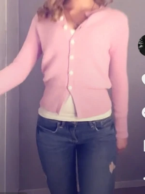 Rosa kofta med pärlknappar från Zara - Supersöt rosa kofta från Zara med långa ärmar och fina pärlformade blomknappar framtill. Koftan är stickad och har en figurnära passform som ger en feminin look. Perfekt att styla med jeans eller kjol för en trendig vibe.