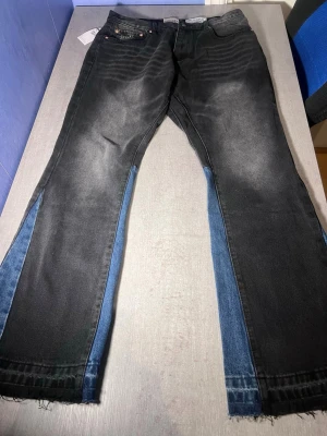 Gallery Dept. svarta jeans med blå paneler - Unika svarta jeans från Gallery Dept. med blå denim-paneler längs sidorna. Raka ben och råa, fransiga benslut ger en cool och avslappnad vibe. Klassisk femficksmodell med knappgylf och detaljerade sömmar. Perfekta för dig som vill sticka ut.