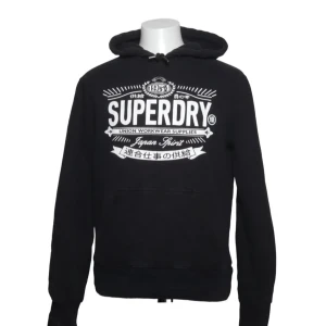 Svart hoodie från Superdry - Snygg svart hoodie från Superdry med stor vit logga och tryck framtill. Finns  tecken på begagnad bild (4). Skriv för minsta lilla fråga!🙏😃