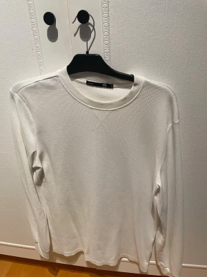 Vit stickad tröja från 157 - Säljer en stilren vit stickad tröja från 157 i storlek S. Tröjan har rund halsringning, diskret X-detalj framtill och är tillverkad i ett mjukt, ribbat material. Perfekt för lager-på-lager och enkel att matcha med andra plagg.