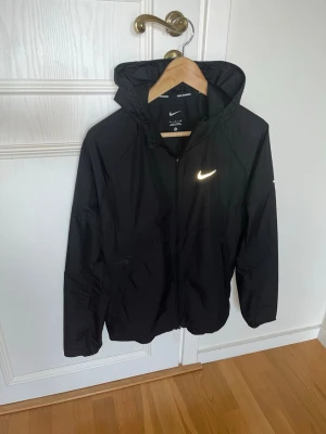 Svart Nike vindjacka med huva - Nu säljer jag min nike miller i mycket bra skick. Självklart äkta nike. Storlek S. Jag är 188 och den är för kort i midjan, skulle rekommendera för dig mellan 170-180. Inga defekter alls.