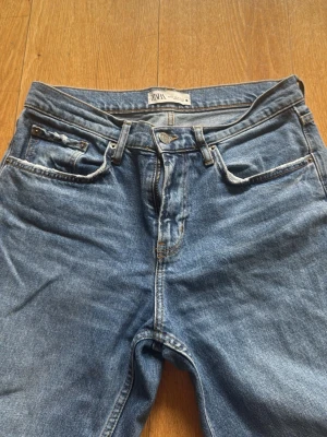 Raka ljus blå Jeans - Säljer ett par klassiska blå jeans från Zara med rak passform och fem fickor. Jeansen har en snygg tvättad look och är tillverkade i denim. Perfekt för dig som gillar en enkel och tidlös stil.