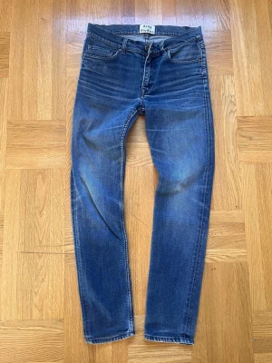 Acne Studios Jeans - Säljer ett par blå slim fit jeans från Acne Studios med klassisk femficksdesign och snygga slitningar. Jeansen har en modern passform och är tillverkade i mjukt denim-material. Perfekta för dig som gillar stilrena och trendiga jeans.