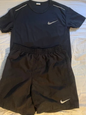 Nike set - Setet innehåller: • T-shirt: Svart med silvrig Nike-swoosh på bröstet och snygga reflexdetaljer på axlarna för extra synlighet. • Shorts: Matchande svarta shorts med elastisk midja och vit Nike-logga nertill. Detaljer: • Märke: Nike • Färg: Svart / Silver • Skick: Jättefint skick, sparsamt använda och stretchiga i materialet. • Storlek: Xs-S  Säljes som set (prioriteras) eller separat vid förfrågan. ⚡️ 