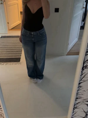 Blåa bootcut jeans med hög midja - Säljer ett par blåa bootcut jeans med hög midja och klassisk femficksdesign. Jeansen har en avslappnad passform och är tillverkade i denim med lätt tvättad look. Perfekta för dig som gillar en tidlös och bekväm stil.
