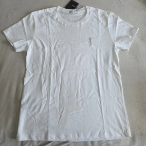 Vit t-shirt från Saint Laurent - Klassisk vit t-shirt från Saint Laurent med diskret logga broderad på bröstet. T-shirten har rund halsringning och korta ärmar. Tillverkad i mjuk bomull för en skön känsla och enkel stil.