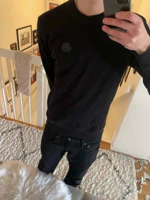 Svart Moncler sweatshirt - Säljer en svart sweatshirt från Moncler med rund halsringning och diskret Moncler-logga på bröstet. Tröjan har en clean och stilren look, perfekt till jeans eller andra byxor. Materialet är mjukt och bekvämt, och modellen är långärmad.