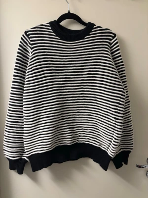 Svartvit randig stickad tröja - En snygg stickad tröja med svartvita horisontella ränder. Tröjan har rund halsringning, långa ärmar och ribbstickade muddar vid ärmslut och nederkant. Perfekt för att skapa en cool och avslappnad look. Materialet är mjukt och bekvämt.
