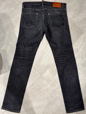Mörkblå jeans från Dsquared - Säljer ett par mörkblå jeans från Dsquared med klassisk femficksdesign och raka ben. Jeansen har kontrastsömmar och en snygg läderpatch bak i midjan. Materialet är slitstark denim och passformen är slim. Perfekt för dig som gillar stilrena och tidlösa jeans.