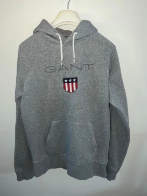 Grå Gant hoodie - Säljer en stilren och bekväm grå hoodie från GANT. Hoodien är ytterst lite använd och är i mycket fint skick, utan några tecken på slitage.  Storlek: M, men skulle även passa dig med storlek S.  Det är bara att höra av sig om du har några frågor eller vill ha fler bilder!