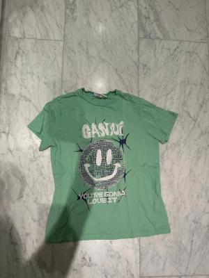 Grön Ganni t-shirt med smileytryck - Cool grön t-shirt från Ganni med stort smileytryck och texten 'You're gonna love it' på framsidan. Tröjan är i mycket bra skick och har storleken XXS.💚💚