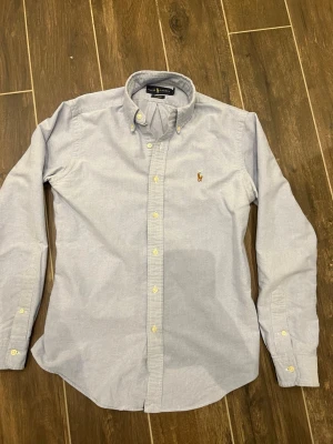 Ljusblå Ralph Lauren skjorta  - Tjena! Säljer denna skjorta då den inte har använts något! Extremt fin i skicket och passar perfekt för de varma sommardagarna med en clean skjorta som passar till allt. Skjortan har storleken S. Vid funderingar och frågor är det bara att höra av sig!