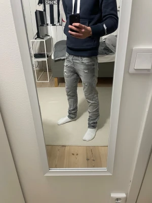 Grå slitna slim fit jeans herr - Säljer ett par grå skinny jeans med slitningar och detaljerade revor framtill. Jeansen har klassisk femficksmodell och bra passform. Perfekta för en avslappnad och trendig stil. w27 men passar w30.