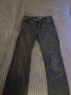 Grå raka jeans med hög midja - Säljer ett par grå jeans med rak passform och hög midja. Klassisk femficksmodell med knapp och dragkedja framtill. Jeansen har en enkel och stilren look, perfekta till en avslappnad outfit. Materialet är denim i bomull.
