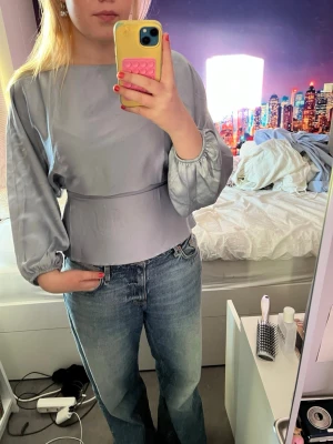 Glansig satinblus - Ljusblå i mjukt satin-liknande material med insnörpt midja och dragkedja i sidan. Snygg till vita jeans typ