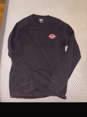 Svart långärmad tröja från Dickies - Säljer en svart långärmad tröja från Dickies med klassisk logga i rött och vitt på bröstet. Tröjan har rund halsringning och är gjord i mjukt bomullsmaterial. Perfekt för en avslappnad och stilren look.