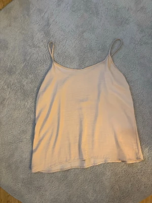 Beige linnetopp med tunna axelband - Enkel och stilren beige linnetopp med tunna axelband och rak passform. Perfekt för varma dagar och lätt att matcha med olika outfits. Materialet känns mjukt och svalt mot huden. Använd få tal gånger!