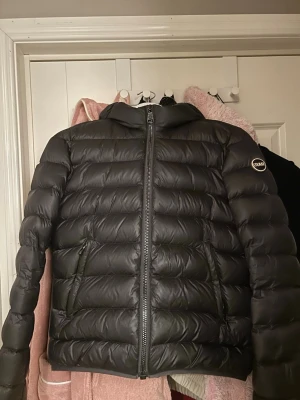 Svart dunjacka med huva Colmar - Snygg svart dunjacka från Colmar med puffig design och huva. Jackan har dragkedja framtill, två sidofickor med dragkedja.