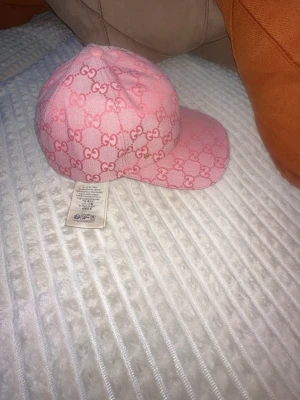  Gucc* keps  - Säljer en rosa keps från Gucc* med det klassiska G monogrammet över hela kepsen. Kepsen har böjd skärm och är tillverkad i ett slitstarkt tygmaterial. Perfekt för dig som vill sticka ut med en lyxig och trendig accessoar.