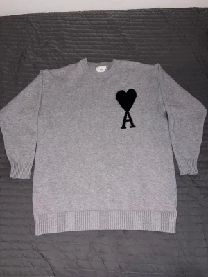 Grå stickad tröja från Ami Paris - Säljer en stilren grå stickad tröja från Ami Paris med svart hjärta och bokstaven A broderat på bröstet. Har haft på din en gång, inte mer för det va inte direkt min typ.