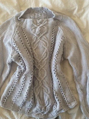 Ljusgrå stickad tröja med flätmönster - Säljer en ljusgrå stickad tröja med snyggt flätmönster och håldetaljer framtill. Tröjan har lång ärm och rund halsringning. Passar både XS och S 🤍🤍🤍
