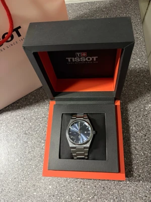 Tissot PRX – Stilren klocka i stål (sprucket glas, fungerar perfekt - Säljer en elegant klocka från Tissot i den populära PRX-stilen.  Klockan fungerar felfritt och håller tiden som den ska. Observera att glaset är sprucket (se bild), men detta påverkar inte funktionen alls – endast kosmetiskt.  Perfekt för dig som vill ha en snygg kvalitetsklocka till ett bättre pris. Levereras med originalbox. 