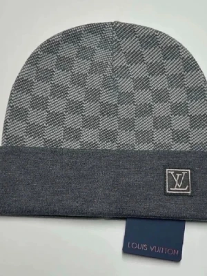 Grå mössa från Louis Vuitton - Snygg grå mössa från Louis Vuitton med uppvikt kant och diskret LV-logga framtill. Tillverkad i mjukt stickat material som känns lyxigt och bekvämt. Perfekt accessoar för att höja din stil under kyliga dagar.