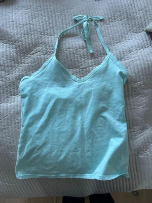 Turkos linnetopp med knyt - Säljer en turkos linnetopp med v-ringning och knyt i nacken. Toppen är ärmlös och har en enkel, clean design som är perfekt för varma dagar. Materialet känns mjukt och lätt, vilket gör den riktigt bekväm att bära.