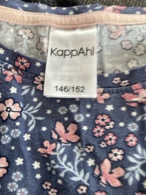 Blommig topp från KappAhl - Söt topp från KappAhl i blått med rosa och vita blommor och fjärilar. Toppen har rund halsringning och är ärmlös, perfekt för varma dagar. Tillverkad i mjuk bomull som känns skön mot huden.