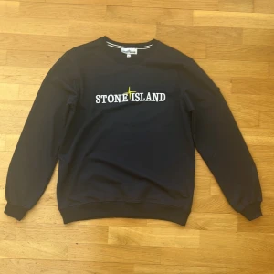 Svart sweatshirt från Stone Island - Svart sweatshirt från Stone Island med rund halsringning och vit logotyp broderad på bröstet. Klassisk passform med ribbade muddar vid ärmslut och nederkant. Perfekt för en avslappnad och stilren look.