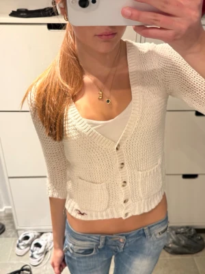 Hollister vit stickad kofta med fickor - Hollister vit stickad kofta med trekvartsärmar.    Storlek S men passar nog XS-S typ!                  Koftan har knappar framtill, två små fickor och ribbade kanter. Perfekt att slänga över ett linne eller t-shirt.    