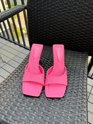 Rosa klackpumps från Boohoo - Säljer ett par trendiga rosa pumps från Boohoo med öppen tå och fyrkantig tåform. Skorna har bred rem över foten och en smal klack. Tillverkade i syntetmaterial med en stilren och modern look. Perfekta för dig som vill sticka ut med färg.