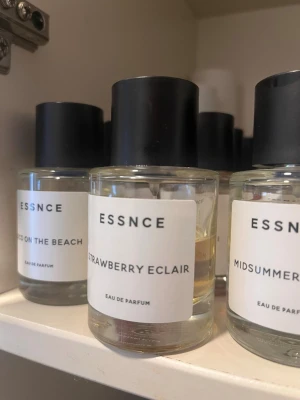 Essnce Strawberry Eclair parfym - Parfymen Strawberry Eclair från Essnce kommer i en rund, genomskinlig glasflaska med svart lock och minimalistisk vit etikett. Doften har en söt och fruktig karaktär, perfekt för dig som gillar bäriga toner. Flaskan har en stilren och modern design.
