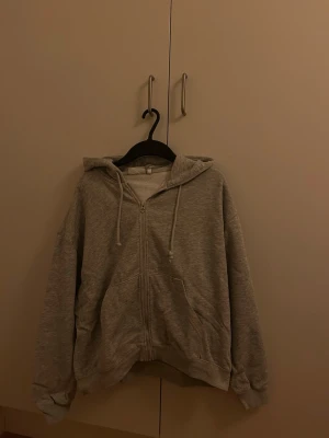 Grå zip hoodie med luva från Weekday - En klassisk grå hoodie med luva och dragkedja från Weekday. Hoodien har två stora fickor framtill och ribbade muddar vid ärmar och nederkant. Tröjan är något oversized. Skriv privat vid frågor! 