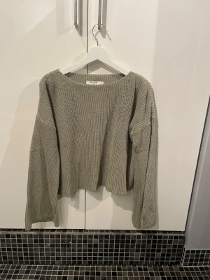 Olivgrön stickad tröja från NA-KD - Säljer en olivgrön stickad tröja från NA-KD med avslappnad passform och bred halsringning. Tröjan har långa ärmar och är gjord i ett mjukt, grovstickat material som passar perfekt till höst och vinter.