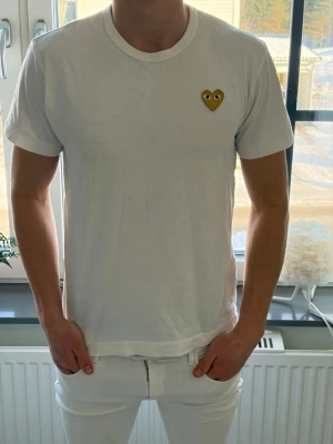 Vit t-shirt med gul hjärtdetalj, cdg - Vit t-shirt från Comme des Garçons Play med en gul hjärtformad patch på bröstet. Klassisk rund halsringning och korta ärmar. Tillverkad i mjuk bomull för en bekväm känsla. Perfekt för en clean och stilren look. Priset är inte hugget i sten✅💎