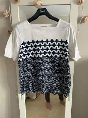 Vit och blå mönstrad  topp från Croft&barrow - Säljer en vit t-shirt från Croft&barrow  med blått geometriskt mönster över hela framsidan och baksidan. T-shirten har rund halsringning och korta ärmar. Perfekt för dig som gillar grafiska prints och vill ha en unik look.
