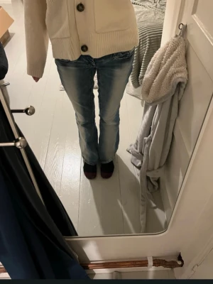 Blå bootcut jeans med låg midja  - Säljer ett par blå bootcut jeans med tydliga slitningar och ljusa tvättade partier framtill. Jeansen har klassisk femficksmodell och låg midja. Perfekta för dig som gillar retrovibbar och en avslappnad stil.