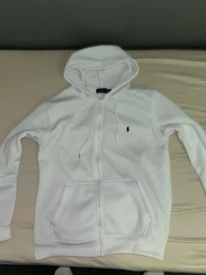 Vit zip hoodie  - Snygg vit hoodie med dragkedja. Klassisk design med huva, dragsnören och två stora fickor framtill. Liten broderad logga på bröstet. Perfekt för lager på lager och chill stil.