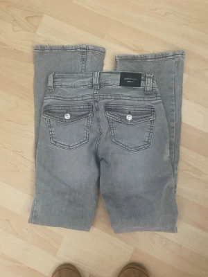 Grå jeans från Perfect Jeans - Snygga grå jeans från Perfect Jeans med raka ben och klassisk femficksmodell. Jeansen har silverfärgade knappar på bakfickorna och bälteshällor. Materialet är mjukt denim som ger en avslappnad look. Perfekta till en streetwear-outfit.