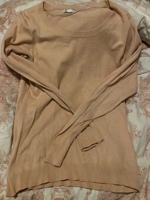 Beige/rosa stickad tröja med rund hals - En enkel och stilren beige/rosa stickad tröja med rund halsringning och långa ärmar. Tröjan har ribbade muddar vid ärmslut och nederkant, vilket ger en snygg passform. Perfekt att matcha med jeans eller kjol för en avslappnad look.                             