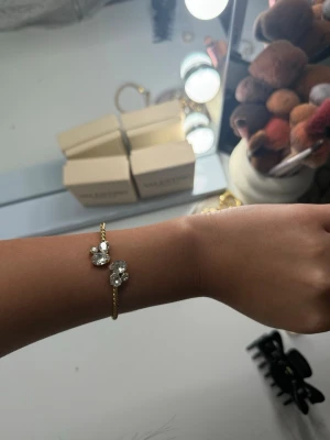 Caroline Svedbom  - Caroline Svedbom armban.  Trendig guldfärgad armband med tvinnad design och flera ljusa, skimrande stenar i olika former framtill. Ringen har en öppen front och ger en elegant men modern känsla. Perfekt för dig som gillar unika detaljer och stilrena accessoarer.
