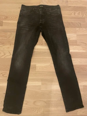 Svarta slim fit jeans från Jack & Jones - Säljer ett par svarta slim fit jeans från Jack & Jones. Jeansen har klassisk femficksdesign, knappgylf och diskreta slitningar framtill för en snygg look. Materialet är stretchigt för extra komfort och passform. Modellen är slim/glenn. Längd är 32