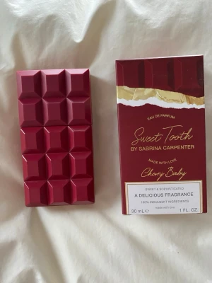 Sweet Tooth Cherry Baby parfym - Unik parfym i form av en mörkröd chokladkaka från Sabrina Carpenter. Doften heter Sweet Tooth Cherry Baby och kommer i en snygg förpackning med gulddetaljer. Flaskan rymmer 30 ml och har en modern, lekfull design som sticker ut i parfymhyllan. Ett fåtal sprut tagna 