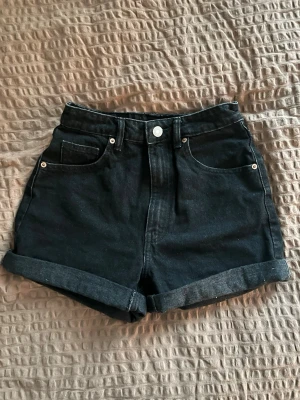 Svarta högmidjade jeansshorts - Säljer ett par svarta högmidjade jeansshorts från Zara. Klassisk femficksmodell med uppvikta benslut. Perfekta till sommaren och lätta att matcha med olika stilar. Tyvärr för små, därmed bara använda några gånger.