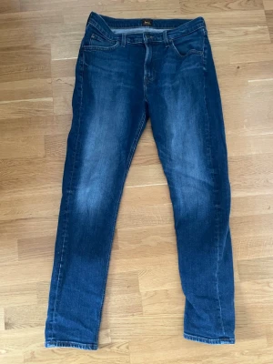 Mörkblå jeans från Lee - Snygga mörkblå slim fit jeans från Lee med klassisk femficksmodell och diskreta slitningar framtill. Jeansen har normal midja, raka ben och är tillverkade i stretchigt denim för extra komfort. Perfekta till en avslappnad look.